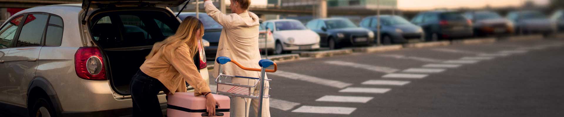 Deux personnes qui chargent une voiture sur le parking d’un aéroport.